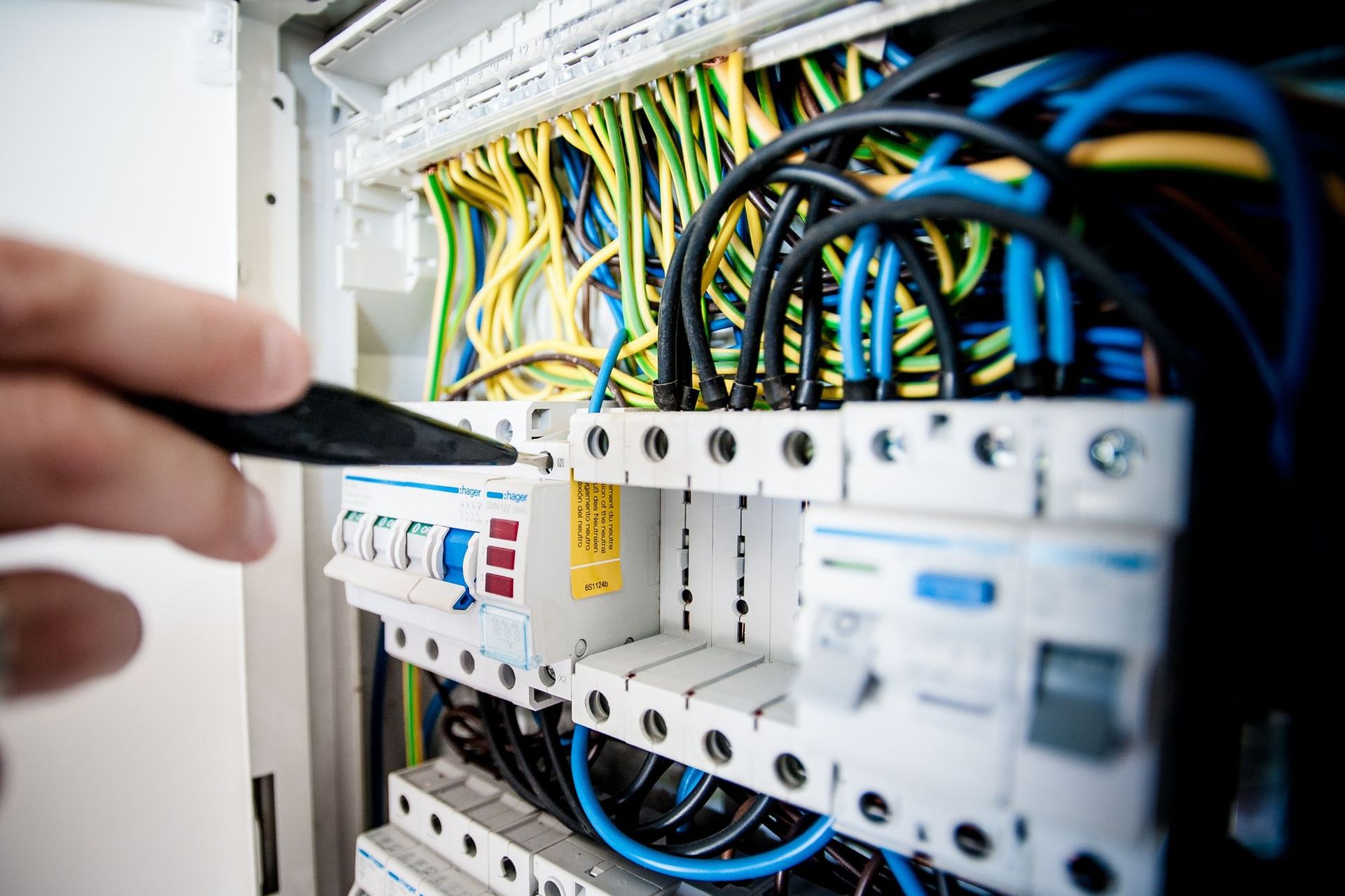 Electrician's hand working on a breaker panel with colorful wiring