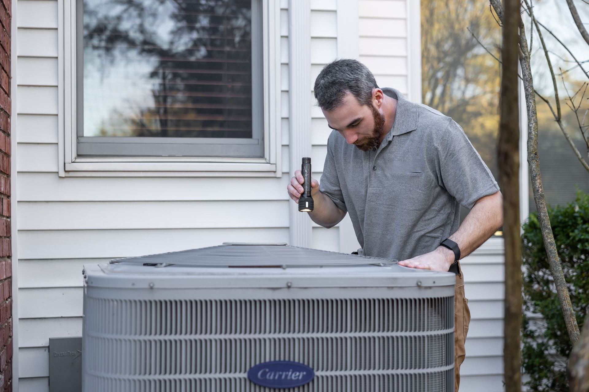 HVAC technician inspecting an outdoor AC condenser with a flashlight