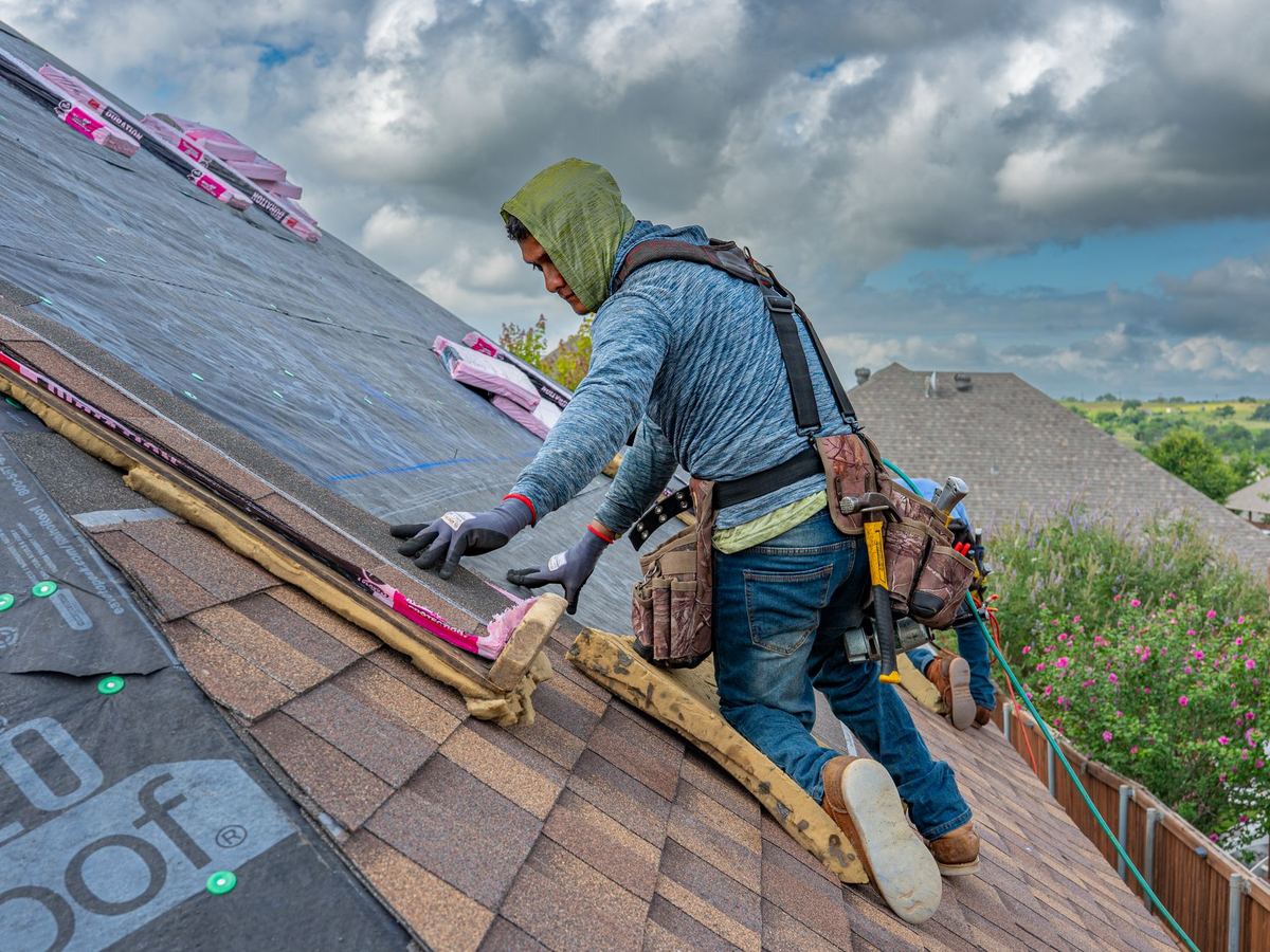 Roofer installing asphalt shingles on a steep roof